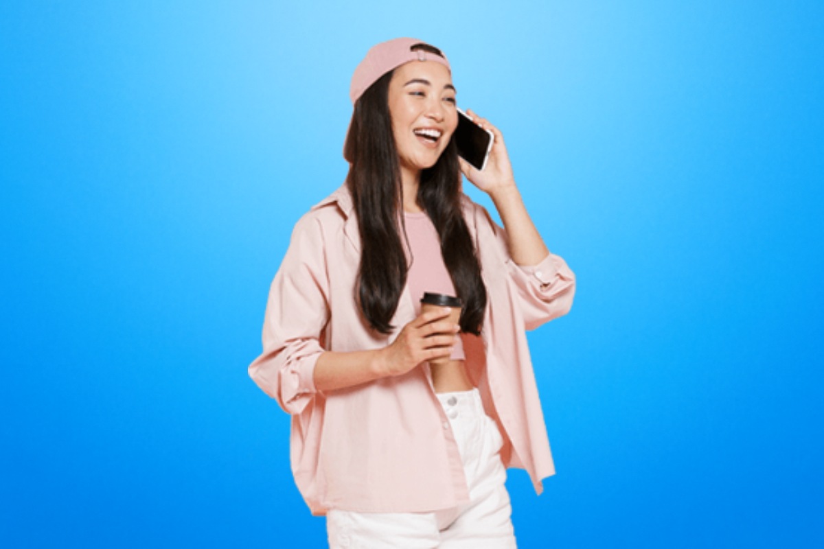 Femme au téléphone avec tasse de café sur fond bleu, sourit grâce au forfait avec option "Booster" de Free à seulement 2€