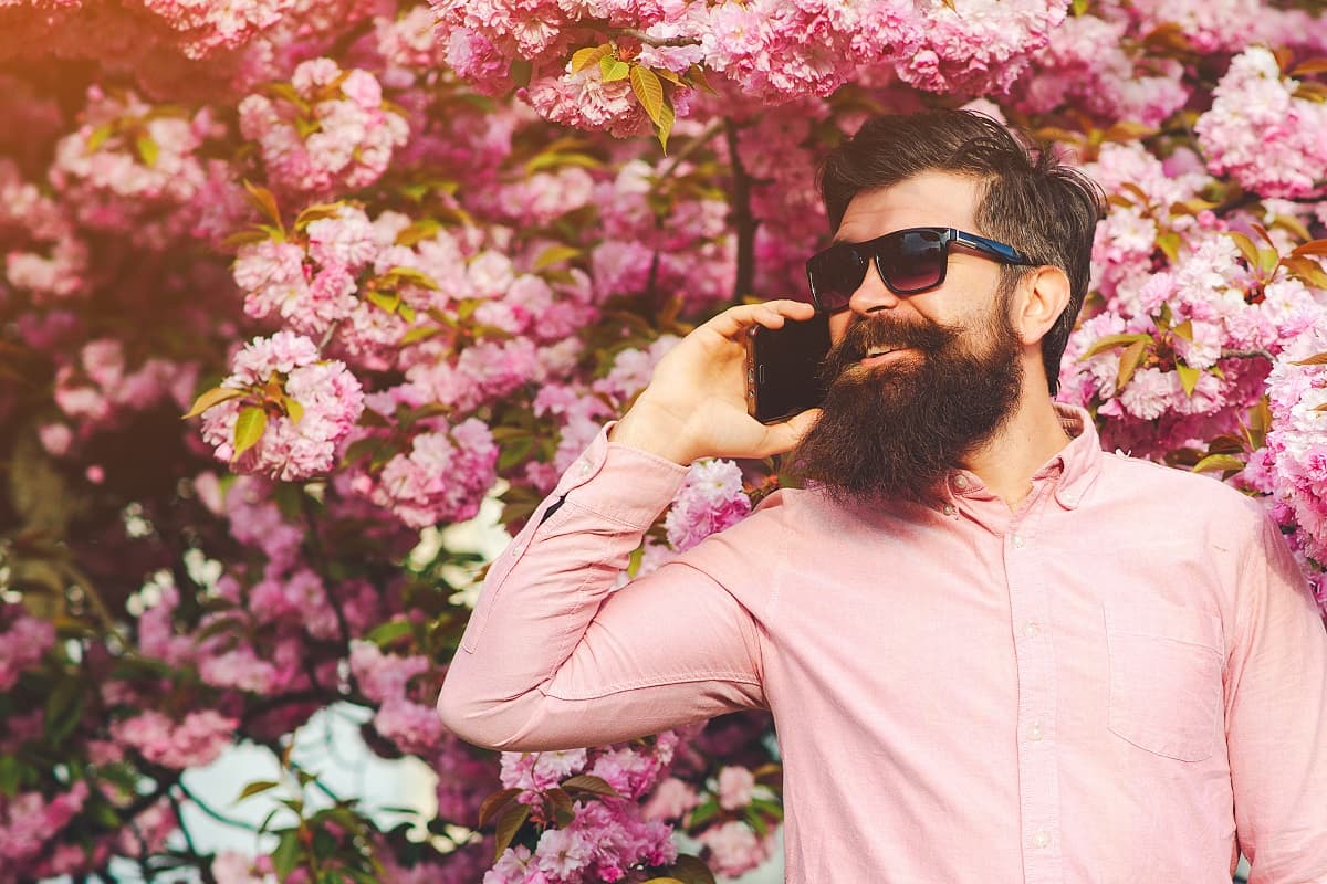 Hipster devant fleurs roses, ravi de son smartphone pas cher avec le coupon de réduction de Rakuten